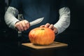Close up of man`s hands carving small orange pumpkin into jack-o-lantern for Halloween holiday decoration with knife Royalty Free Stock Photo