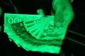 A close up of a man`s hands holding Canadian money under a green light- $100 bill