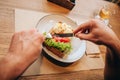 Close up of man`s hands holding fork and knofe and cutting dish into two pieces. There is a cup of tea on right side Royalty Free Stock Photo