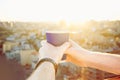 Close up man`s hands holding take away paper cup with morning hot drink - coffee or tea with inspiring view on abstract city back