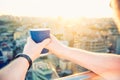 Close up man`s hands holding take away paper cup with morning hot drink - coffee or tea with inspiring view on abstract city back Royalty Free Stock Photo