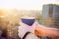 Close up man`s hands holding take away paper cup with morning hot drink - coffee or tea with inspiring view on abstract city back Royalty Free Stock Photo