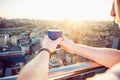 Close up man`s hands holding take away paper cup with morning hot drink - coffee or tea with inspiring view on abstract city back Royalty Free Stock Photo