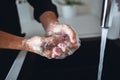 Close up of man`s hands in soap foam. Washing fingers and palms and cleaning them. Water pouring out of tap into sink in