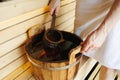 Close-up of a man in a sauna scooping water with a ladle from a wooden bucket.