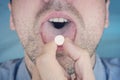 Close up man taking pill medicine. young man put in your mouth yellow pill  on blue background. Taking Royalty Free Stock Photo