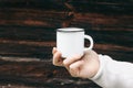 Close up of man travelers hand holding metal mug with hot drink. Outdoor tea, coffee relax time. Mockup of white enamel Royalty Free Stock Photo