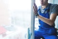 Close-up of a man in uniform and blue gloves washes a windows with window scraper. Professional home cleaning service Royalty Free Stock Photo