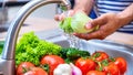 Close-up of man washing vegetables in kitchen sink with water.