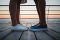 Close up of man and woman hipster couple feet in sneakers at the beach at sunrise sky at wooden deck summer time, at yellow blue e