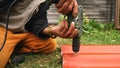 Close-up of man in working clothes and gold watch on the hand drilling red metal tile on the ground. Clip. Materials and