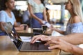 Close Up Of Man Working On Laptop In Foreground With Women Meeting Behind In Busy Coffee Shop Royalty Free Stock Photo