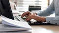 Close-up of a man& x27;s hands typing on a laptop keyboard, with a stack of paperwork beside them. AI generated Royalty Free Stock Photo