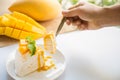 Close up mango crepe cake sliced on a white plate with a woman hand holding a spoon with a piece of cake and sliced mango fruits