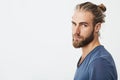 Close up of manly handsome guy with fashionable hairstyle and beard looking in camera, holding head in three quarters