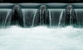 Close up of a manmade concrete weir in a city with a blue river cascading over it Royalty Free Stock Photo