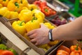 Close up of mans hands with fitness tracker picking out yellow peppers in the fresh vegetable section of a grocery store Royalty Free Stock Photo