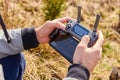 Close up mans hands holding drone remote controller with smartphone in the field. Concept of aerial shooting and flying