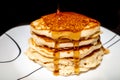 Close up of Maple syrup pouring onto fluffy hotcakes on a white plate.