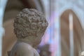 Close up of marble statue back of head of small child, cherub, showing curly hair detail. Cathedral wall with prism