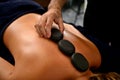 Close-up of masseur laying hot stones along spine of young woman. Ayurvedic hot stone massage in modern spa salon Royalty Free Stock Photo