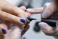 Close-up, the master evens the color of the manicure with blue, applying gel polish on it with a brush