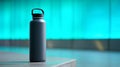 Matte black reusable water bottle with handle cap on concrete surface against blurred turquoise background in soft natural light Royalty Free Stock Photo