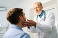 Close-up of mature adult male doctor otolaryngologist touching lymph nodes on neck and examining throat of male patient Royalty Free Stock Photo