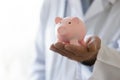 Close up mature doctor holding pink piggy bank, medical insurance