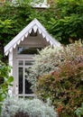 Close up of mature front garden full of shrubs with characterful porch with white painted canopy over, in Kew, London UK