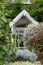 Close up of mature front garden full of shrubs with characterful porch with white painted canopy over, in Kew, London UK