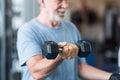 Close up of mature man holding two dumbbells doing exercise at the gym to be healthy and fitness - portrait of active senior Royalty Free Stock Photo