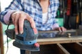 Close Up Mature Woman Upcycling Furniture In Workshop At Home Using Electric Sander