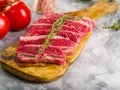 Close-up. Meat raw steaks with a sprig of rosemary on a cutting board, ripe red tomatoes, spices, seasonings on a gray background Royalty Free Stock Photo