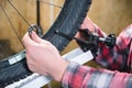 Close-up of men`s hands with a specialized wrench on a stand in the workshop tightening the spokes of the wheel