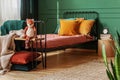 Close-up of a frame bed for a child with orange pillows standing against green wall in bright bedroom interior. Real photo