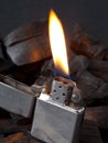 Close-up of metal gas lighter with burning fire on dark coal background