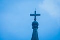 Close up metal holy cross or crucifix on the top of white church with blue sky in the background.