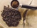 Close up of metal portafilter filled with coffee powder and coffee beans around on wooden table Royalty Free Stock Photo