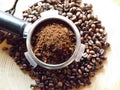 Close up of metal portafilter filled with coffee powder and coffee beans around on wooden table Royalty Free Stock Photo