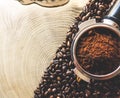 Close up of metal portafilter filled with coffee powder and coffee beans around on wooden table Royalty Free Stock Photo