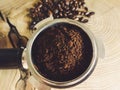 Close up of metal portafilter filled with coffee powder and coffee beans around on wooden table Royalty Free Stock Photo