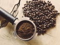 Close up of metal portafilter filled with coffee powder and coffee beans around on wooden table Royalty Free Stock Photo