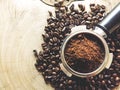 Close up of metal portafilter filled with coffee powder and coffee beans around on wooden table Royalty Free Stock Photo