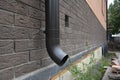 A close-up on a metal rain gutter downpipe, downspout of a roof gutter system and a foundation vent of a new house