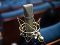 Close-up of a microphone against a backdrop of a row of blue theater chairs on a stage