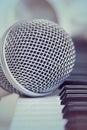 Close up on a microphone during recording session with a singer, piano in the background, music studio.