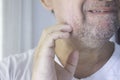 Close up of a middle-aged Latino man scratching his jaw. Barely grown beard. Gray beard