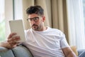 Close-up of a middle-aged man sitting at home on the sofa and holding a digital tablet in his hand Royalty Free Stock Photo