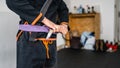 Close up on midsection of unknown bjj brazilian jiu jitsu athlete tie up purple belt on the kimono gi uniform at the academy